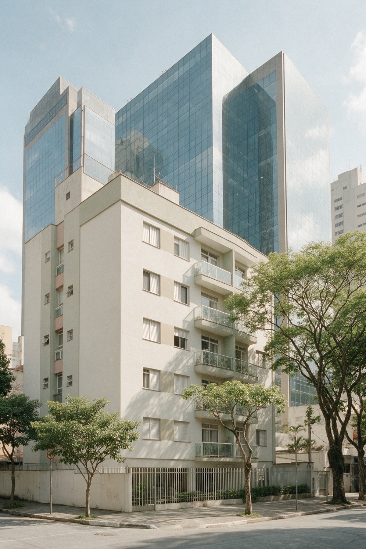 Torres de escritório de vidro da Vila Olímpia vistas de baixo, com um prédio residencial mais baixo à frente e árvores na calçada